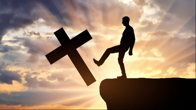 Homem ateu empurra o símbolo da cruz cristã - Getty Images